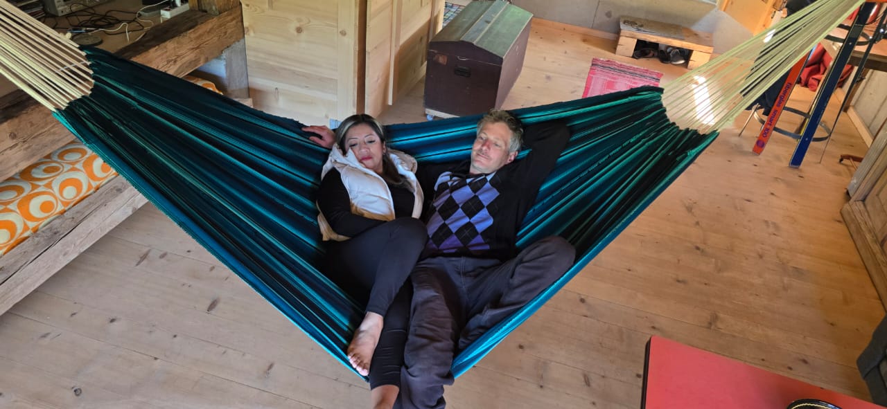 Two people from up lying in a large green fabric hammock made on wooden looms